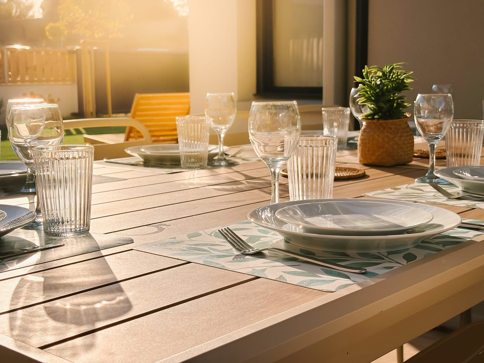 Table dressée en contre-jour — verres, assiettes et chemins de table.