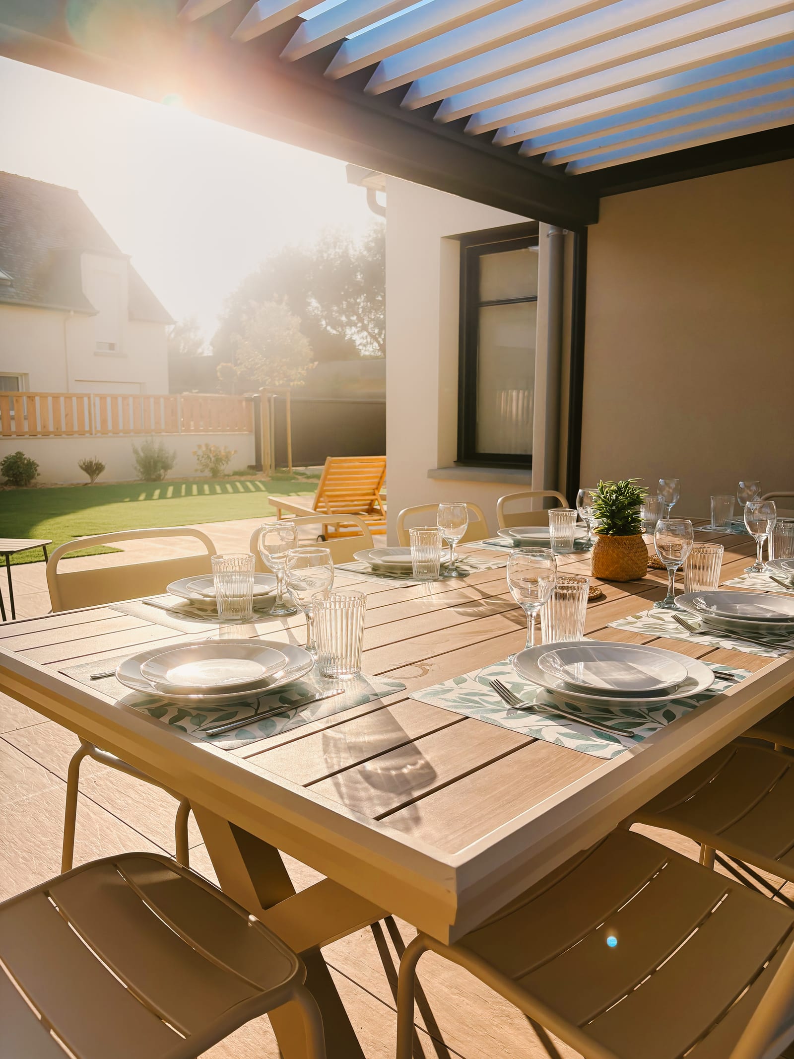 Repas sous la pergola, pelouse et balancelle en arrière-plan.