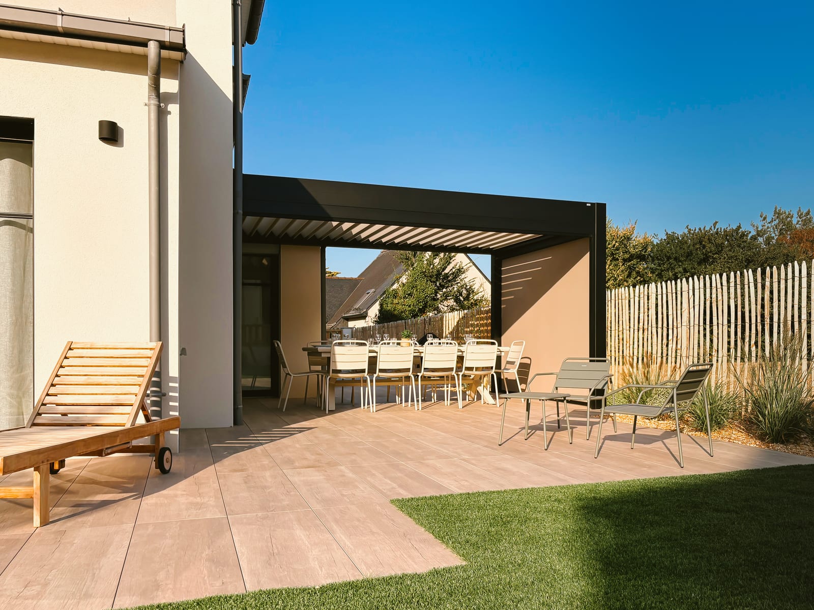 Terrasse depuis le jardin : bain de soleil, coin repas sous pergola et clôture en châtaignier.
