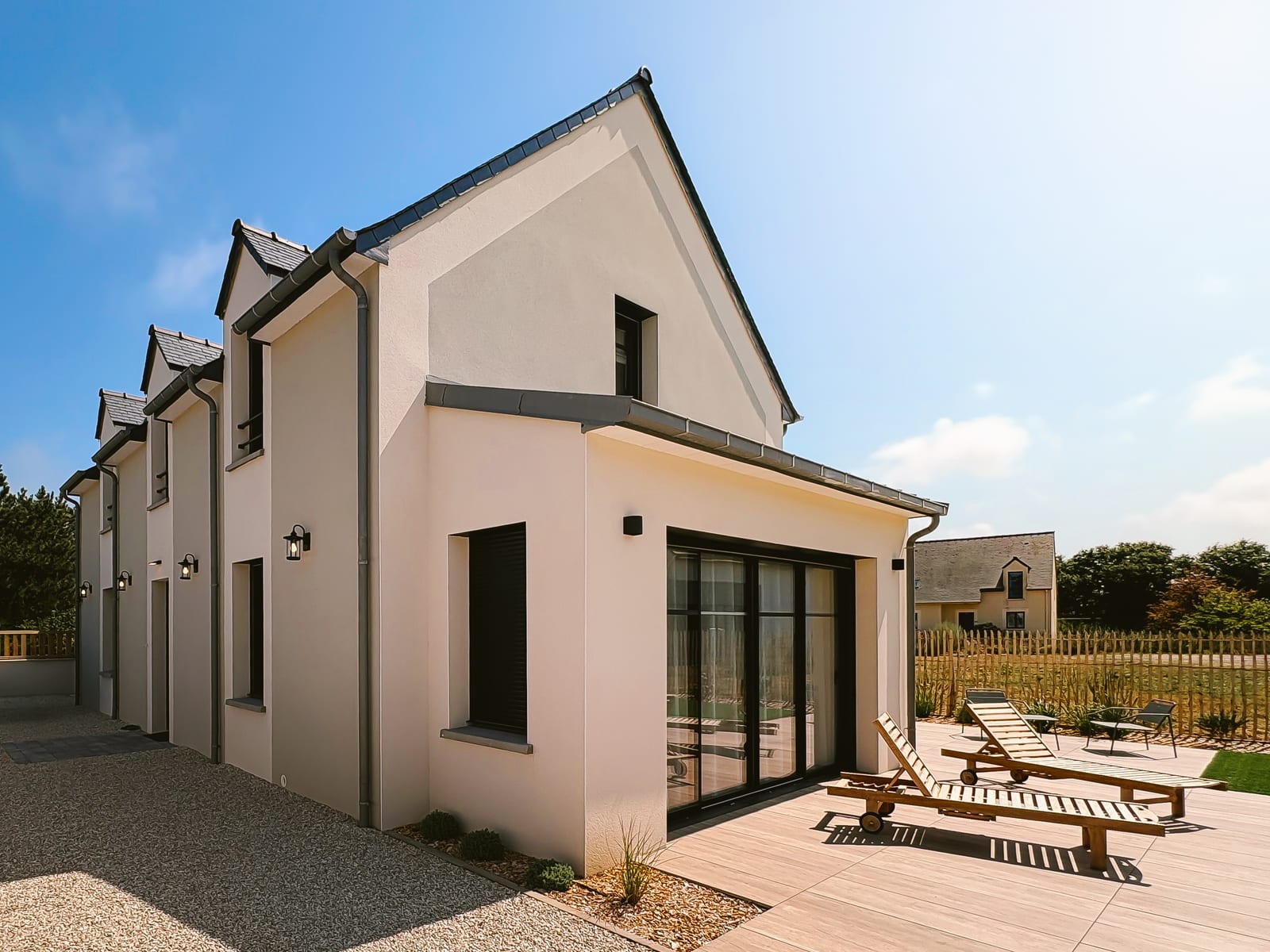 La maison vue depuis le fond du jardin, ses trois pignons et la terrasse.